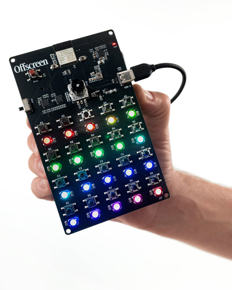 Offscreen screen-free handheld game device held in one hand, showing its black PCB with 20 rainbow light-up buttons, rotary dial, and USB-C cable